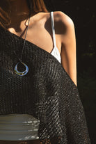 Woman wearing TIC TOC TC31650-SOLENA SOLENA crystal sequin crochet poncho featuring lightweight open crochet knit fabric, allover crystal sequin embellishments, a wide off-shoulder neckline, relaxed draped poncho silhouette, cropped asymmetrical hem, and thin tassel fringe detail, styled over a fitted inner layer for a western festival and vacation-ready look.