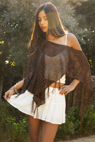 Woman wearing TIC TOC TC31650-SOLENA SOLENA crystal sequin crochet poncho featuring lightweight open crochet knit fabric, allover crystal sequin embellishments, a wide off-shoulder neckline, relaxed draped poncho silhouette, cropped asymmetrical hem, and thin tassel fringe detail, styled over a fitted inner layer for a western festival and vacation-ready look.