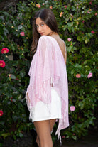 Woman wearing TIC TOC TC31650-SOLENA SOLENA crystal sequin crochet poncho featuring lightweight open crochet knit fabric, allover crystal sequin embellishments, a wide off-shoulder neckline, relaxed draped poncho silhouette, cropped asymmetrical hem, and thin tassel fringe detail, styled over a fitted inner layer for a western festival and vacation-ready look.