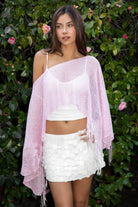 Woman wearing TIC TOC TC31650-SOLENA SOLENA crystal sequin crochet poncho featuring lightweight open crochet knit fabric, allover crystal sequin embellishments, a wide off-shoulder neckline, relaxed draped poncho silhouette, cropped asymmetrical hem, and thin tassel fringe detail, styled over a fitted inner layer for a western festival and vacation-ready look.