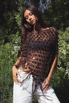 Woman wearing TIC TOC TC31690-LUNARA LUNARA sequin crochet fringe poncho featuring open crochet knit fabric, large allover sequin embellishments, a scalloped wide neckline worn off one shoulder, relaxed poncho silhouette, triangle point hem, and long fringe tassel trim, styled over a fitted top for a western festival and vacation-ready boho look.