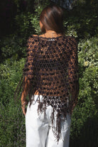 Woman wearing TIC TOC TC31690-LUNARA LUNARA sequin crochet fringe poncho featuring open crochet knit fabric, large allover sequin embellishments, a scalloped wide neckline worn off one shoulder, relaxed poncho silhouette, triangle point hem, and long fringe tassel trim, styled over a fitted top for a western festival and vacation-ready boho look.
