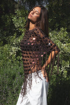 Woman wearing TIC TOC TC31690-LUNARA LUNARA sequin crochet fringe poncho featuring open crochet knit fabric, large allover sequin embellishments, a scalloped wide neckline worn off one shoulder, relaxed poncho silhouette, triangle point hem, and long fringe tassel trim, styled over a fitted top for a western festival and vacation-ready boho look.