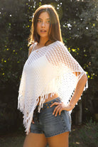 Woman wearing TIC TOC TC31801-TIVONA TIVONA open crochet fringe poncho featuring lightweight open crochet knit fabric, a wide off shoulder neckline, relaxed draped poncho silhouette, symmetrical triangle hem shape, sheer breathable texture, and tassel fringe hem detail, styled over a fitted inner layer for a western boho vacation look.