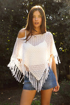 Woman wearing TIC TOC TC31801-TIVONA TIVONA open crochet fringe poncho featuring lightweight open crochet knit fabric, a wide off shoulder neckline, relaxed draped poncho silhouette, symmetrical triangle hem shape, sheer breathable texture, and tassel fringe hem detail, styled over a fitted inner layer for a western boho vacation look.
