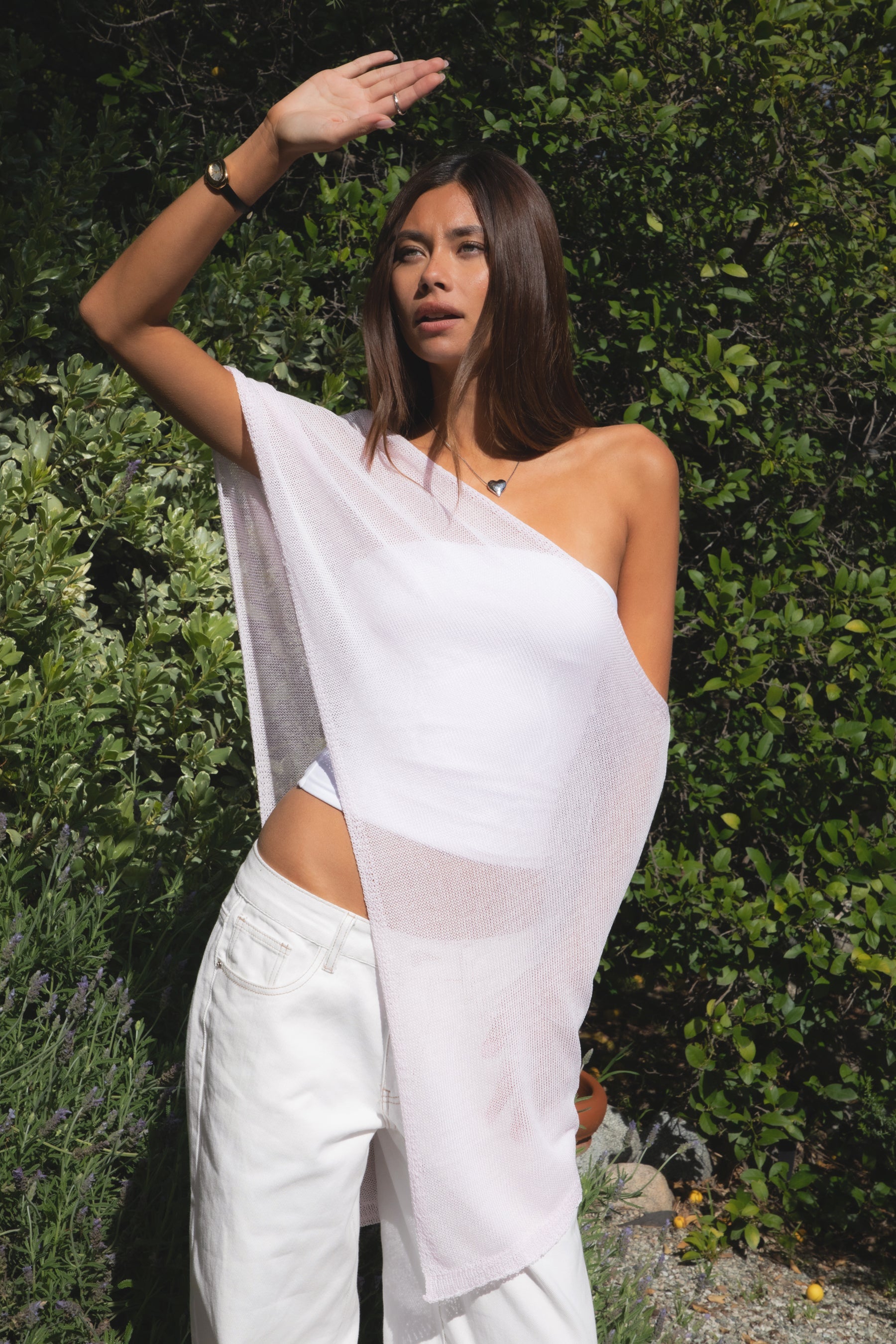 Woman wearing TIC TOC TC31873 SOLEI lightweight open sheer sweater knit poncho in PINK, featuring a wide off-shoulder neckline, airy open knit texture, relaxed draped poncho silhouette, and asymmetrical hem, styled over a white cami with light wash denim for a western-casual summer layering look.
