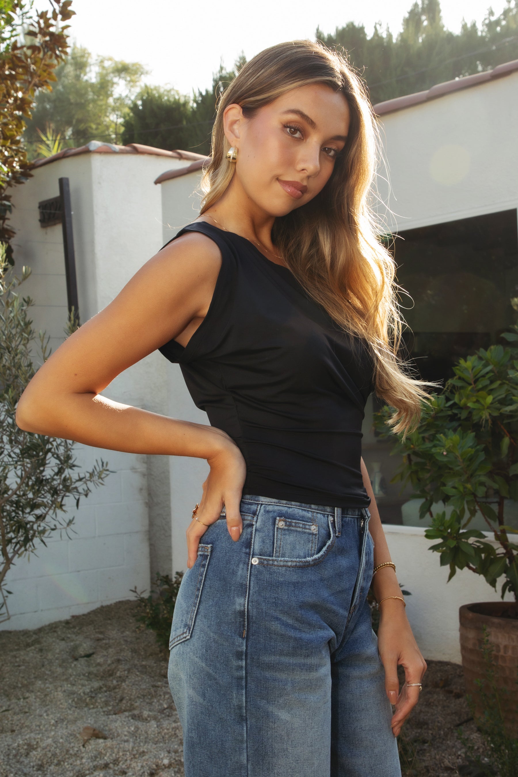 Woman wearing TIC TOC TC31874-ETOILE ETOILE asymmetrical off-the-shoulder top featuring a slash neck off-shoulder neckline, draped asymmetrical overlay front, cinched waist with ruched side detailing, and a fitted body-hugging shape in smooth stretch milk jersey, styled with high-rise bottoms for a sleek Y2K-inspired going-out look.