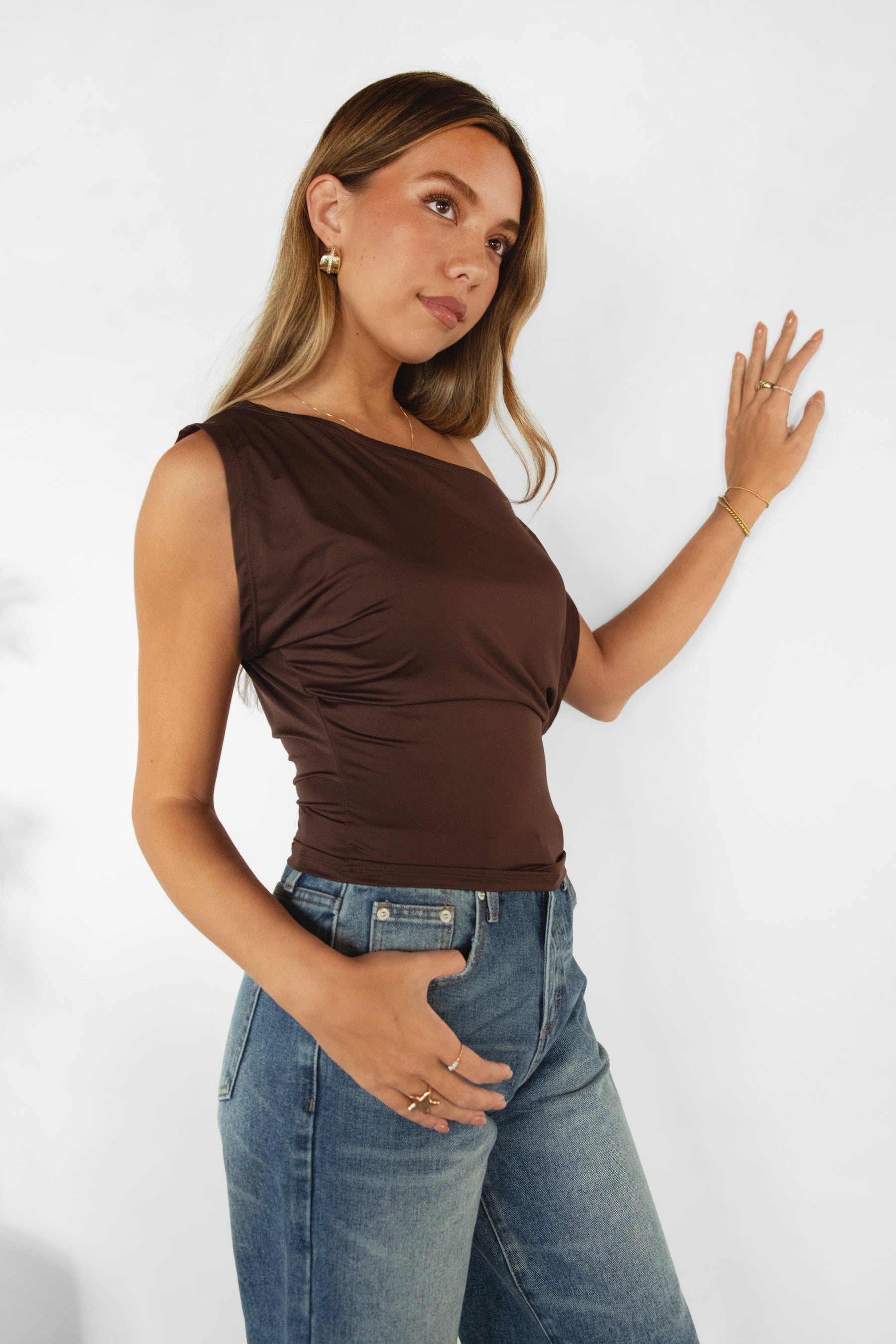 Woman wearing TIC TOC TC31874-ETOILE ETOILE asymmetrical off-the-shoulder top featuring a slash neck off-shoulder neckline, draped asymmetrical overlay front, cinched waist with ruched side detailing, and a fitted body-hugging shape in smooth stretch milk jersey, styled with high-rise bottoms for a sleek Y2K-inspired going-out look.