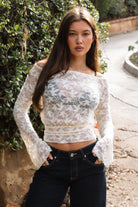 Woman wearing TC31934-VELORA floral lace off-shoulder top with bell sleeves and cropped slim fit body, styled with high-rise bottoms for a boho Y2K going-out look.