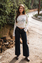 Woman wearing TC31934-VELORA floral lace off-shoulder top with bell sleeves and cropped slim fit body, styled with high-rise bottoms for a boho Y2K going-out look.