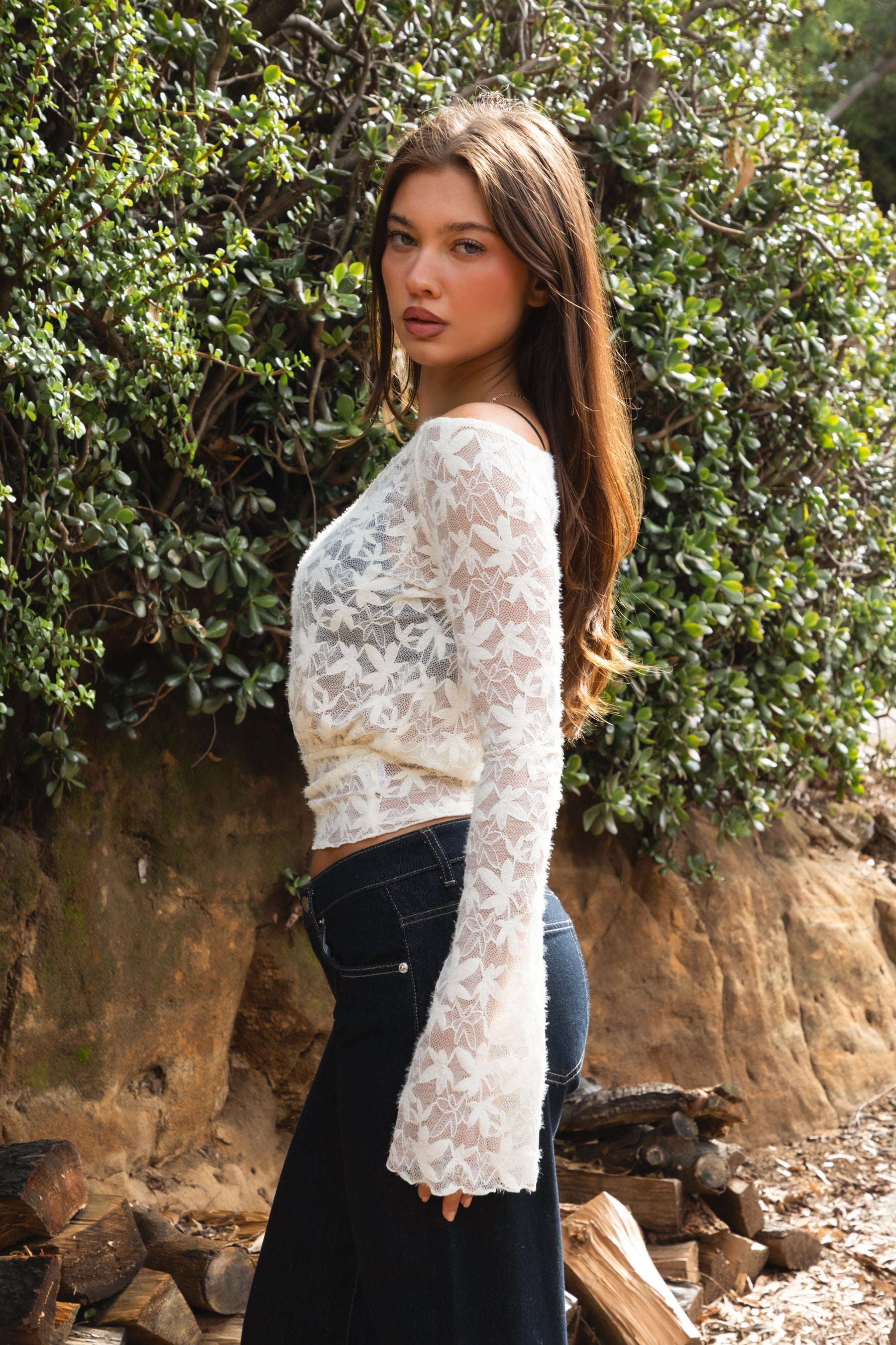 Woman wearing TC31934-VELORA floral lace off-shoulder top with bell sleeves and cropped slim fit body, styled with high-rise bottoms for a boho Y2K going-out look.