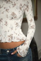 Woman wearing TIC TOC TC31955 MAEVA boat neck mesh print smocked long sleeve top featuring soft stretch smocked fabric with an allover floral print, cropped body-hugging fit, high boat neckline, and long sleeves with subtle ruffle hem and cuffs for a romantic modern western-inspired look.