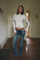 Woman wearing TIC TOC TC31955 MAEVA boat neck mesh print smocked long sleeve top featuring soft stretch smocked fabric with an allover floral print, cropped body-hugging fit, high boat neckline, and long sleeves with subtle ruffle hem and cuffs for a romantic modern western-inspired look.