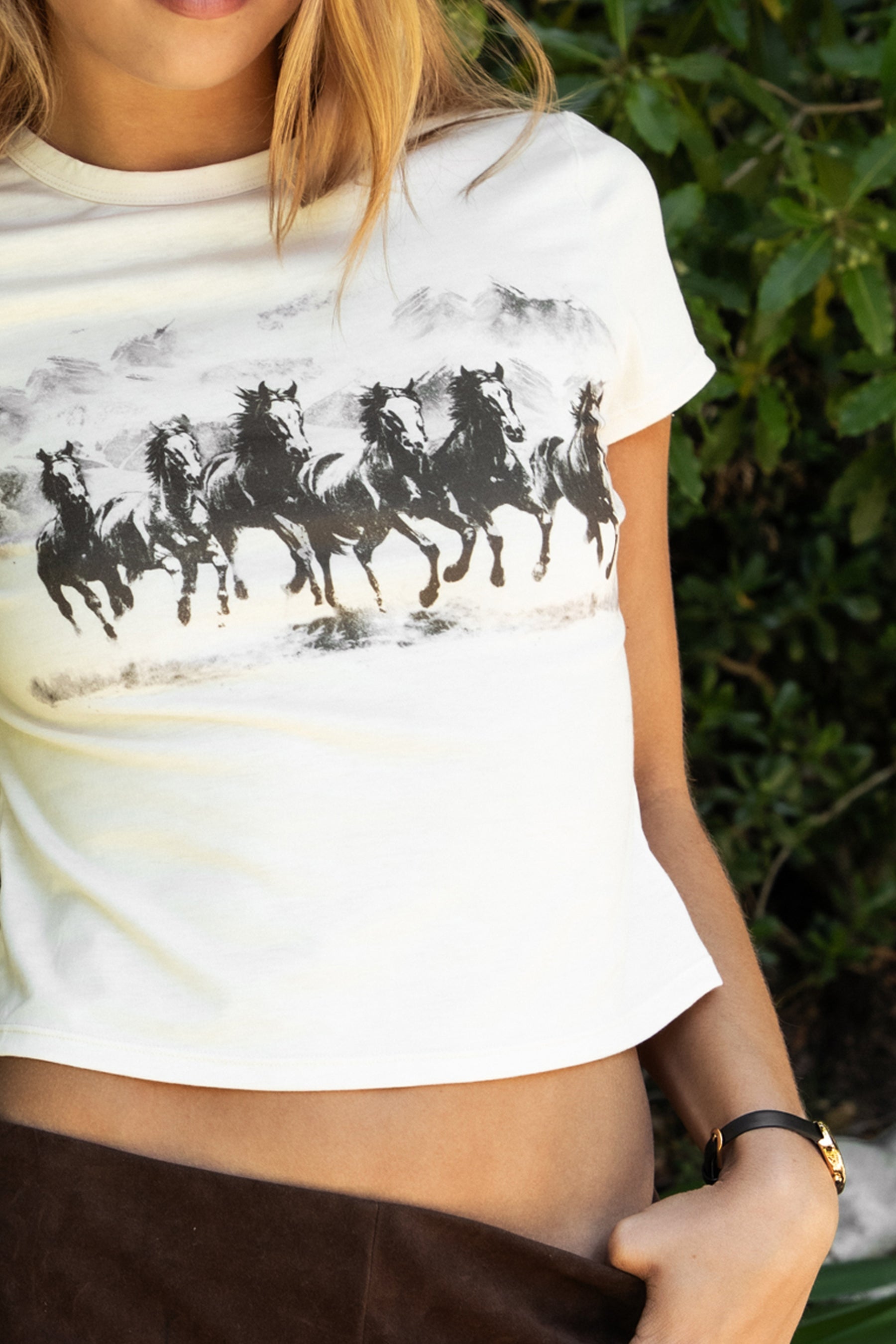 Woman wearing BRONWEN western graphic cropped baby tee featuring soft stretch single jersey fabric, classic round neckline, short sleeves, monotone horse graphic, and a cropped body-hugging silhouette for everyday casual styling.