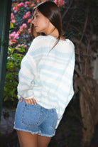 Woman wearing TIC TOC TC31973-ROMY ROMY Rodeo Girl stripe knit sweater featuring a lightweight open crochet knit in soft blue and white stripes, heart-framed “Rodeo Girl” front crochet embroidery, relaxed oversized silhouette, long sleeves with ribbed cuffs, and a classic crew neckline, styled with denim bottoms for a western casual, campus-ready summer layering look.