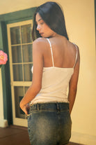 Woman wearing TIC TOC TC32064 MIA stretch jacquard jersey cropped tank top featuring a V neckline with lace trim, front tie detail at the bust, slim fitted silhouette, and cropped lettuce hem, styled with casual bottoms for a feminine Y2K-inspired summer look.