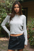 Woman wearing TIC TOC TC32069 KRISTY cable knit basic long sleeve cardigan top featuring a soft lightweight cotton cable knit texture, round neckline, full front button closure, slim fit silhouette, and semi-cropped length for a polished preppy everyday look.