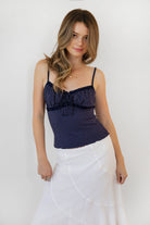 Woman wearing LOTTIE polka dot print lace contrast jersey tank featuring a delicate polka dot print, V-neckline with self-tie bow detail, lace trim along the neckline and under bust, adjustable thin straps, and a soft stretch jersey body-skimming silhouette.