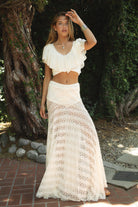 Woman wearing ELOWIN ruffled V-neck short sleeve crop top featuring lightweight yoryu chiffon, V-neckline at front and back with picot lace trim, flowy ruffled sleeves, halter style self tie back strap, and a cropped inner lining for support with a sheer layered finish.
