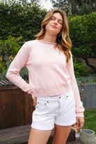 Woman wearing LUMEE rolled neck long sleeve knit sweater featuring a minimal rolled neckline, soft cotton knit fabric, long sleeves with ribbed cuffs and hem, center back seam detail, and a relaxed cropped fit for easy everyday layering.