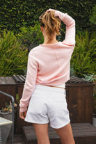 Woman wearing LUMEE rolled neck long sleeve knit sweater featuring a minimal rolled neckline, soft cotton knit fabric, long sleeves with ribbed cuffs and hem, center back seam detail, and a relaxed cropped fit for easy everyday layering.