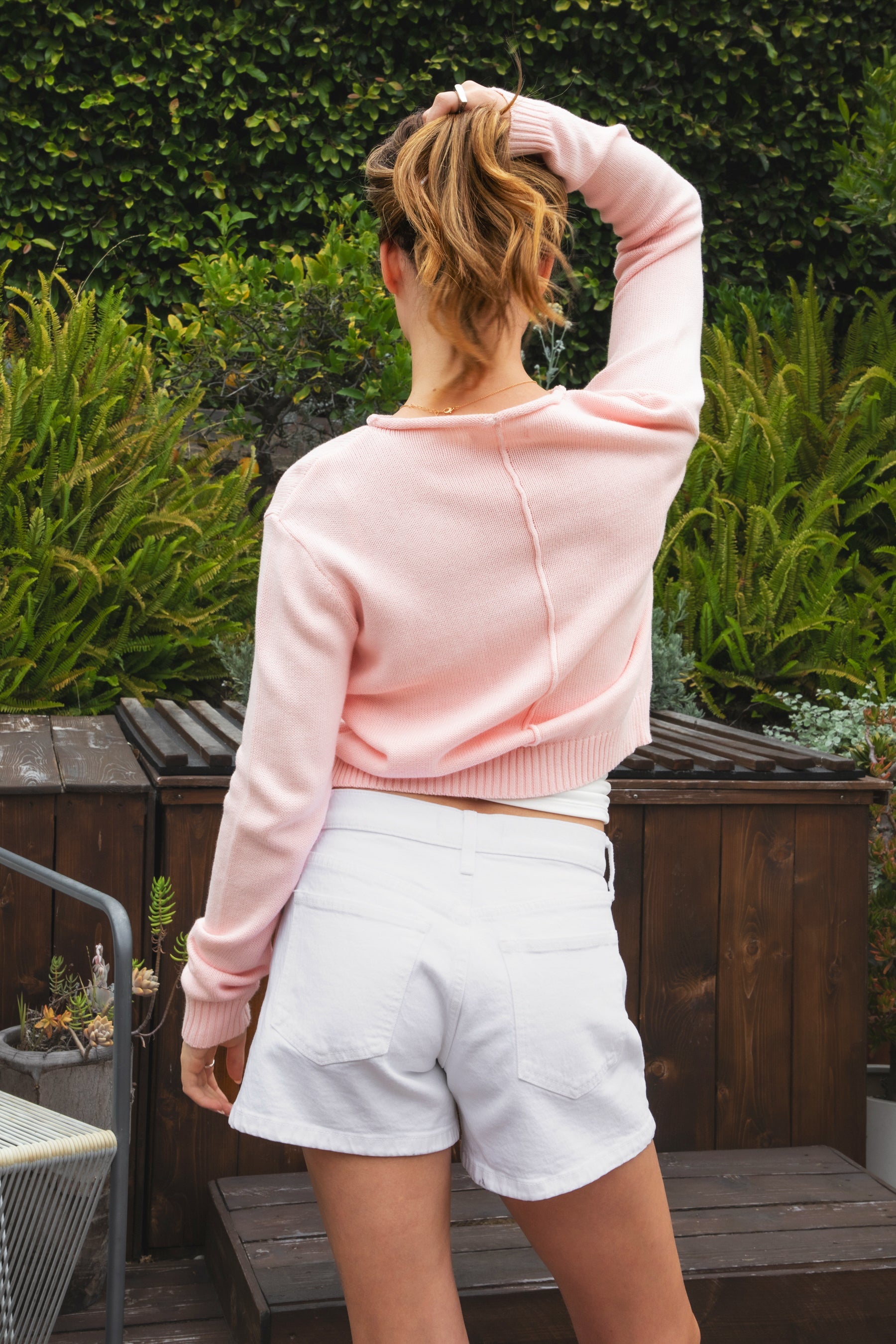 Woman wearing LUMEE rolled neck long sleeve knit sweater featuring a minimal rolled neckline, soft cotton knit fabric, long sleeves with ribbed cuffs and hem, center back seam detail, and a relaxed cropped fit for easy everyday layering.