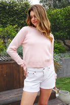 Woman wearing LUMEE rolled neck long sleeve knit sweater featuring a minimal rolled neckline, soft cotton knit fabric, long sleeves with ribbed cuffs and hem, center back seam detail, and a relaxed cropped fit for easy everyday layering.