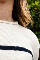 Woman wearing WINSLOW striped cable knit long sleeve sweater featuring a classic rolled neckline, contrast stripe design, soft cotton cable knit fabric, long sleeves with ribbed cuffs and hem, and a relaxed mid-length silhouette for effortless everyday layering.