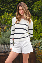 Woman wearing WINSLOW striped cable knit long sleeve sweater featuring a classic rolled neckline, contrast stripe design, soft cotton cable knit fabric, long sleeves with ribbed cuffs and hem, and a relaxed mid-length silhouette for effortless everyday layering.