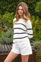 Woman wearing WINSLOW striped cable knit long sleeve sweater featuring a classic rolled neckline, contrast stripe design, soft cotton cable knit fabric, long sleeves with ribbed cuffs and hem, and a relaxed mid-length silhouette for effortless everyday layering.