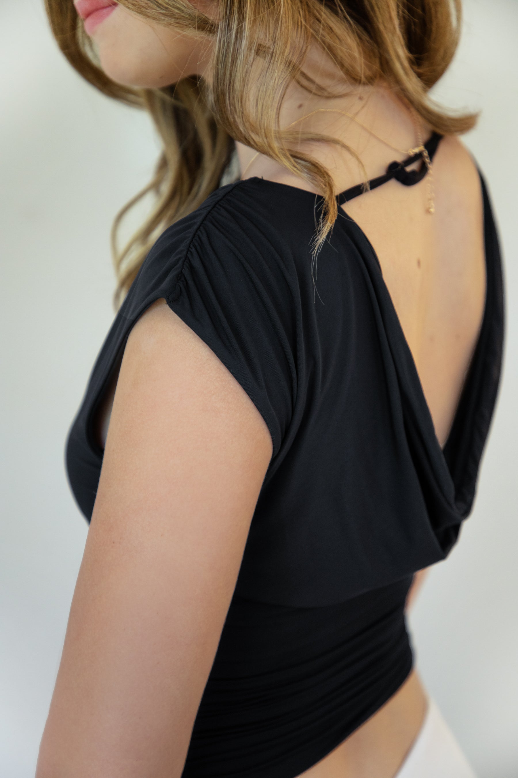 Woman wearing SELENE boat neck cowl back side tie crop top featuring an elegant boat neckline, draped cowl back, adjustable back strap, side tie ruching details, cap short sleeves, and lightweight stretch jersey fabric for a feminine cropped silhouette.