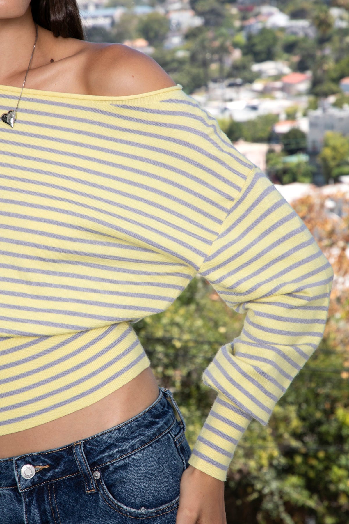 Woman wearing BELLAMY roll neck stripe off shoulder sweater top featuring soft stripe sweater knit fabric, off shoulder neckline, relaxed long sleeve silhouette, cropped hem, wide ribbed waistband, and smooth stretch feel for cozy lounge and travel styling.