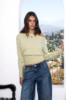 Woman wearing BELLAMY roll neck stripe off shoulder sweater top featuring soft stripe sweater knit fabric, off shoulder neckline, relaxed long sleeve silhouette, cropped hem, wide ribbed waistband, and smooth stretch feel for cozy lounge and travel styling.
