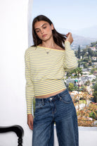 Woman wearing BELLAMY roll neck stripe off shoulder sweater top featuring soft stripe sweater knit fabric, off shoulder neckline, relaxed long sleeve silhouette, cropped hem, wide ribbed waistband, and smooth stretch feel for cozy lounge and travel styling.