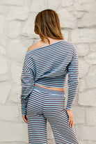 Woman wearing BELLAMY roll neck stripe off shoulder sweater top featuring soft stripe sweater knit fabric, off shoulder neckline, relaxed long sleeve silhouette, cropped hem, wide ribbed waistband, and smooth stretch feel for cozy lounge and travel styling.