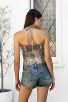 Woman wearing GLITZWOOD camo sequin lace up corset top featuring allover woodland camo print, shimmering sequin overlay, front lace up detail with metal eyelets, halter neck tie design, structured fitted corset silhouette, back zipper closure, and fully lined interior for smooth comfort.