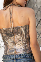 Woman wearing GLITZWOOD camo sequin lace up corset top featuring allover woodland camo print, shimmering sequin overlay, front lace up detail with metal eyelets, halter neck tie design, structured fitted corset silhouette, back zipper closure, and fully lined interior for smooth comfort.