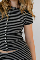 Woman wearing VELA stripe jersey short sleeve top featuring a classic stripe print, boat neckline, front button detail, short cap sleeves, and soft stretch jersey fabric designed to pair with the coordinating VELA micro shorts for relaxed lounge styling.