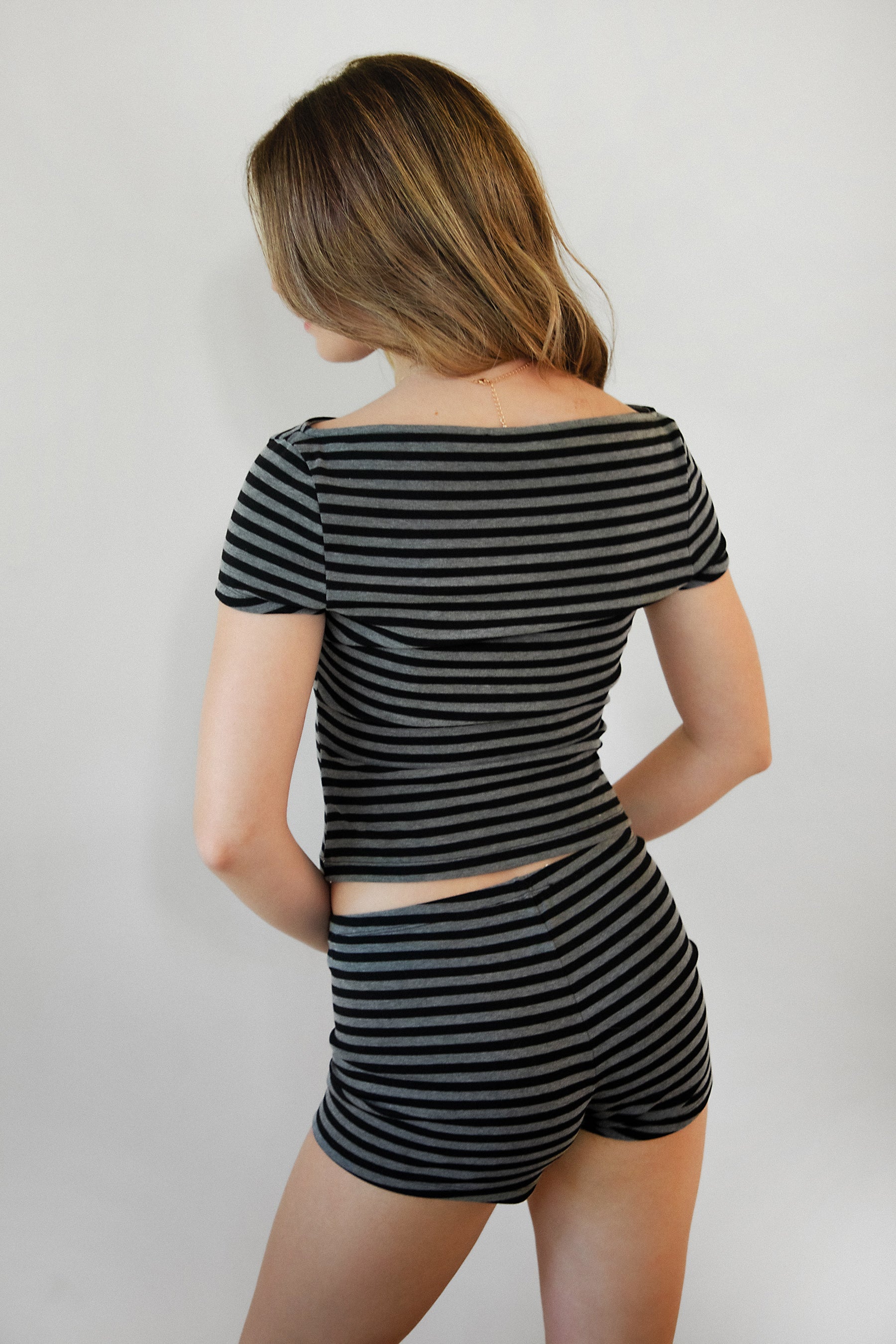 Woman wearing VELA stripe jersey short sleeve top featuring a classic stripe print, boat neckline, front button detail, short cap sleeves, and soft stretch jersey fabric designed to pair with the coordinating VELA micro shorts for relaxed lounge styling.