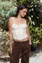Woman wearing ELISHA ruffled lace up chiffon cropped corset top featuring softly textured chiffon fabric, gathered bust, delicate ruffle trim neckline, adjustable self tie shoulder straps, vertical ruffle detailing, fitted cropped bodice, open back with adjustable lace up closure, and soft jersey lining.