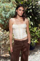 Woman wearing ELISHA ruffled lace up chiffon cropped corset top featuring softly textured chiffon fabric, gathered bust, delicate ruffle trim neckline, adjustable self tie shoulder straps, vertical ruffle detailing, fitted cropped bodice, open back with adjustable lace up closure, and soft jersey lining.