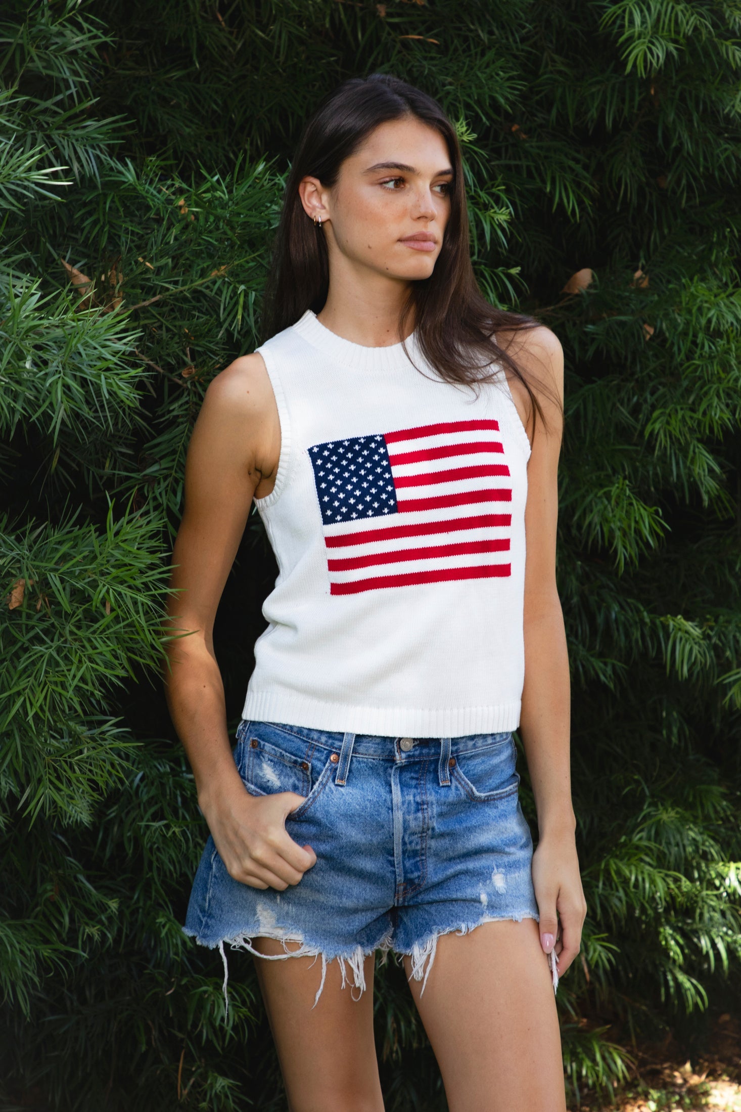 Woman wearing LIBBY American flag sweater knit tank featuring soft breathable 100% cotton sweater knit fabric, clean fitted silhouette, classic crew neckline, sleeveless design, American flag knit graphic across the front, ribbed trim along the neckline and armholes, and ribbed hem for a structured finish.
