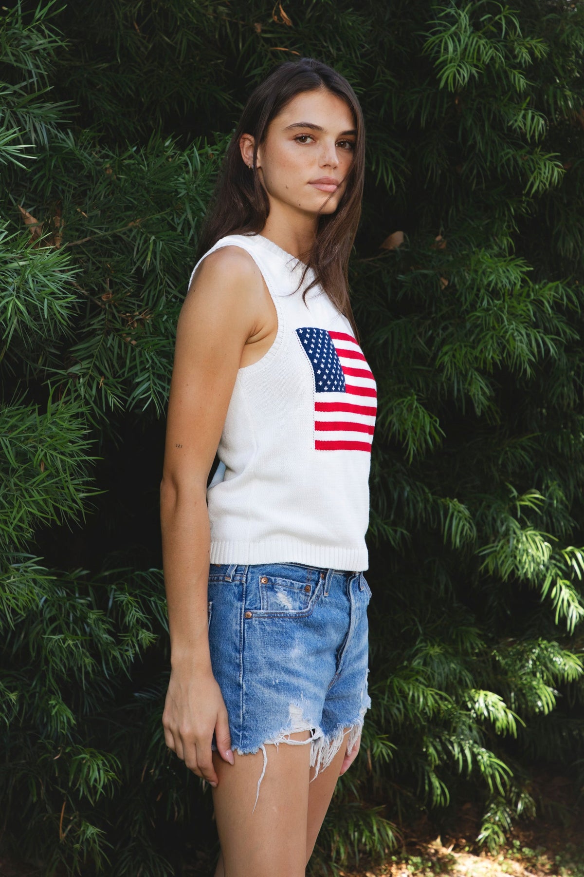 Woman wearing LIBBY American flag sweater knit tank featuring soft breathable 100% cotton sweater knit fabric, clean fitted silhouette, classic crew neckline, sleeveless design, American flag knit graphic across the front, ribbed trim along the neckline and armholes, and ribbed hem for a structured finish.