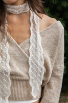 Woman wearing ELIA embroidered lace thin scarf featuring delicate sheer crochet lace fabric, intricate diamond pattern embroidery, soft textured dotted embroidery details, narrow skinny scarf silhouette, scalloped lace trim along both edges, and long tapered ends for a romantic vintage inspired look.