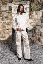Woman wearing ALBA embroidered wide leg denim pants featuring structured cotton blend denim, high rise waist, classic four pocket design, intricate floral eyelet embroidery throughout the legs, relaxed wide leg silhouette, full length fit, button and zip fly closure, and belt loops along the waistline.