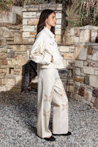 Woman wearing ALBA embroidered wide leg denim pants featuring structured cotton blend denim, high rise waist, classic four pocket design, intricate floral eyelet embroidery throughout the legs, relaxed wide leg silhouette, full length fit, button and zip fly closure, and belt loops along the waistline.
