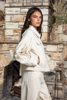 Woman wearing ALBA embroidered wide leg denim pants featuring structured cotton blend denim, high rise waist, classic four pocket design, intricate floral eyelet embroidery throughout the legs, relaxed wide leg silhouette, full length fit, button and zip fly closure, and belt loops along the waistline.