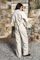 Woman wearing ALBA embroidered wide leg denim pants featuring structured cotton blend denim, high rise waist, classic four pocket design, intricate floral eyelet embroidery throughout the legs, relaxed wide leg silhouette, full length fit, button and zip fly closure, and belt loops along the waistline.