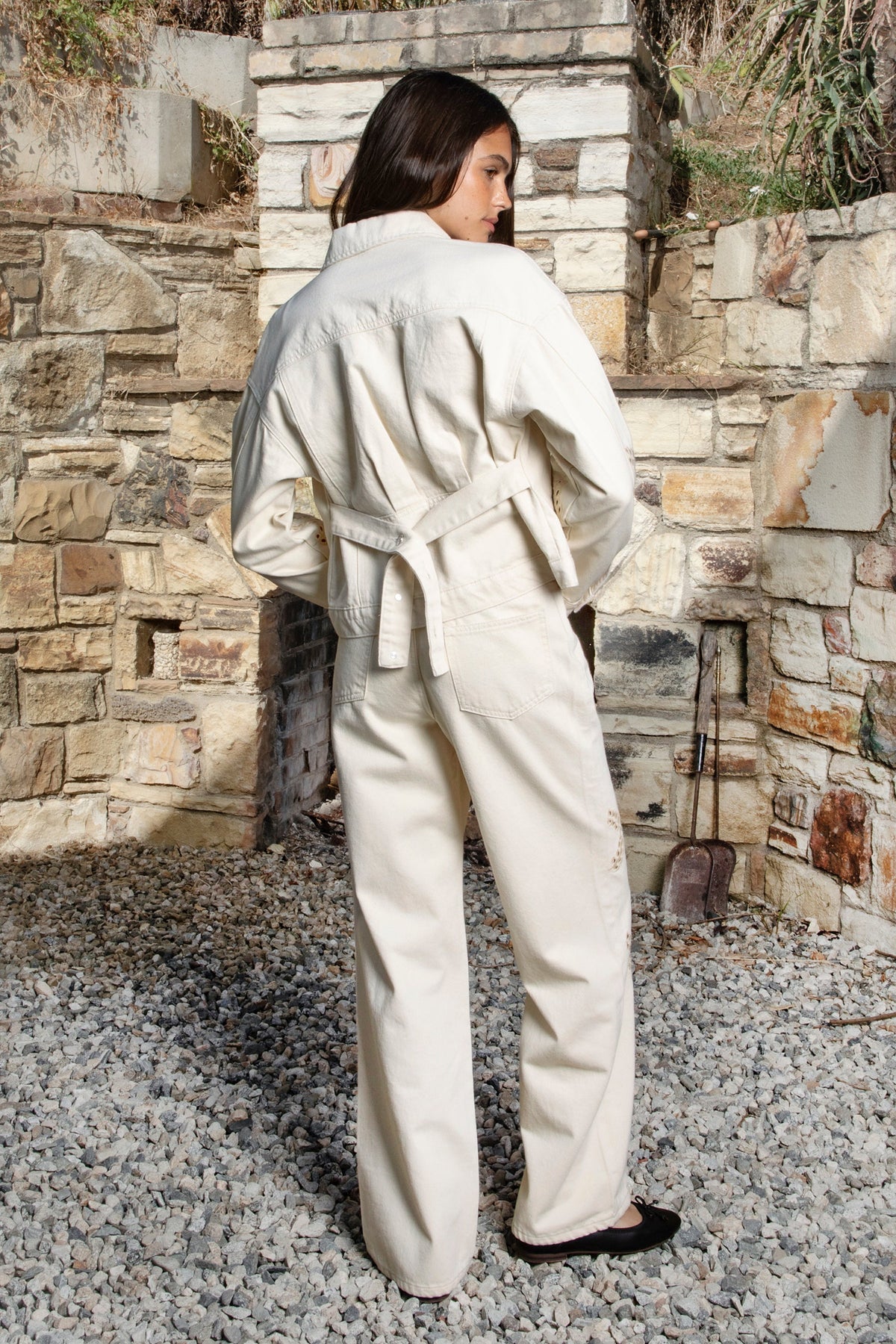 Woman wearing ALBA embroidered wide leg denim pants featuring structured cotton blend denim, high rise waist, classic four pocket design, intricate floral eyelet embroidery throughout the legs, relaxed wide leg silhouette, full length fit, button and zip fly closure, and belt loops along the waistline.