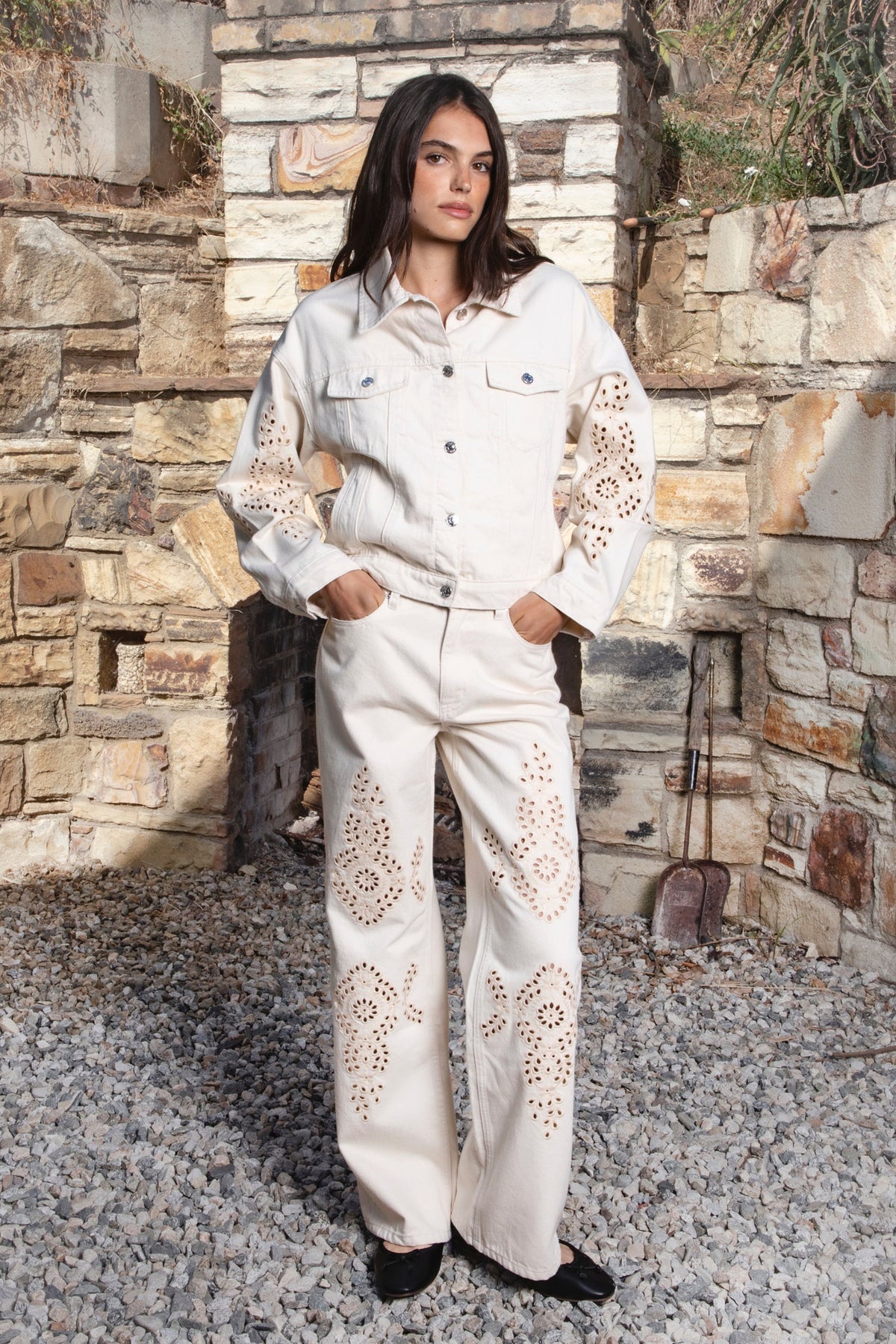 Woman wearing ALBA embroidered wide leg denim pants featuring structured cotton blend denim, high rise waist, classic four pocket design, intricate floral eyelet embroidery throughout the legs, relaxed wide leg silhouette, full length fit, button and zip fly closure, and belt loops along the waistline.